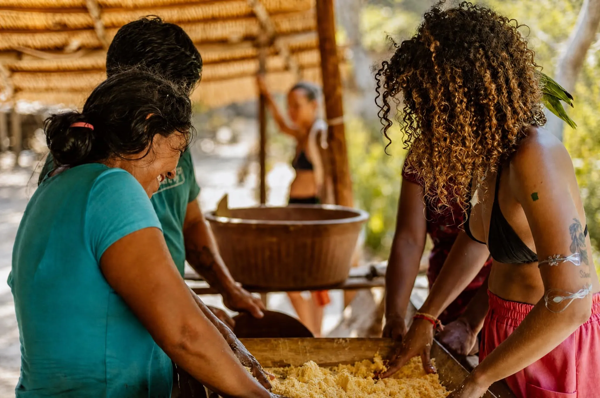 Moradores da comunidade e hóspedes em volta de um cocho, peneirando a massa de mandioca