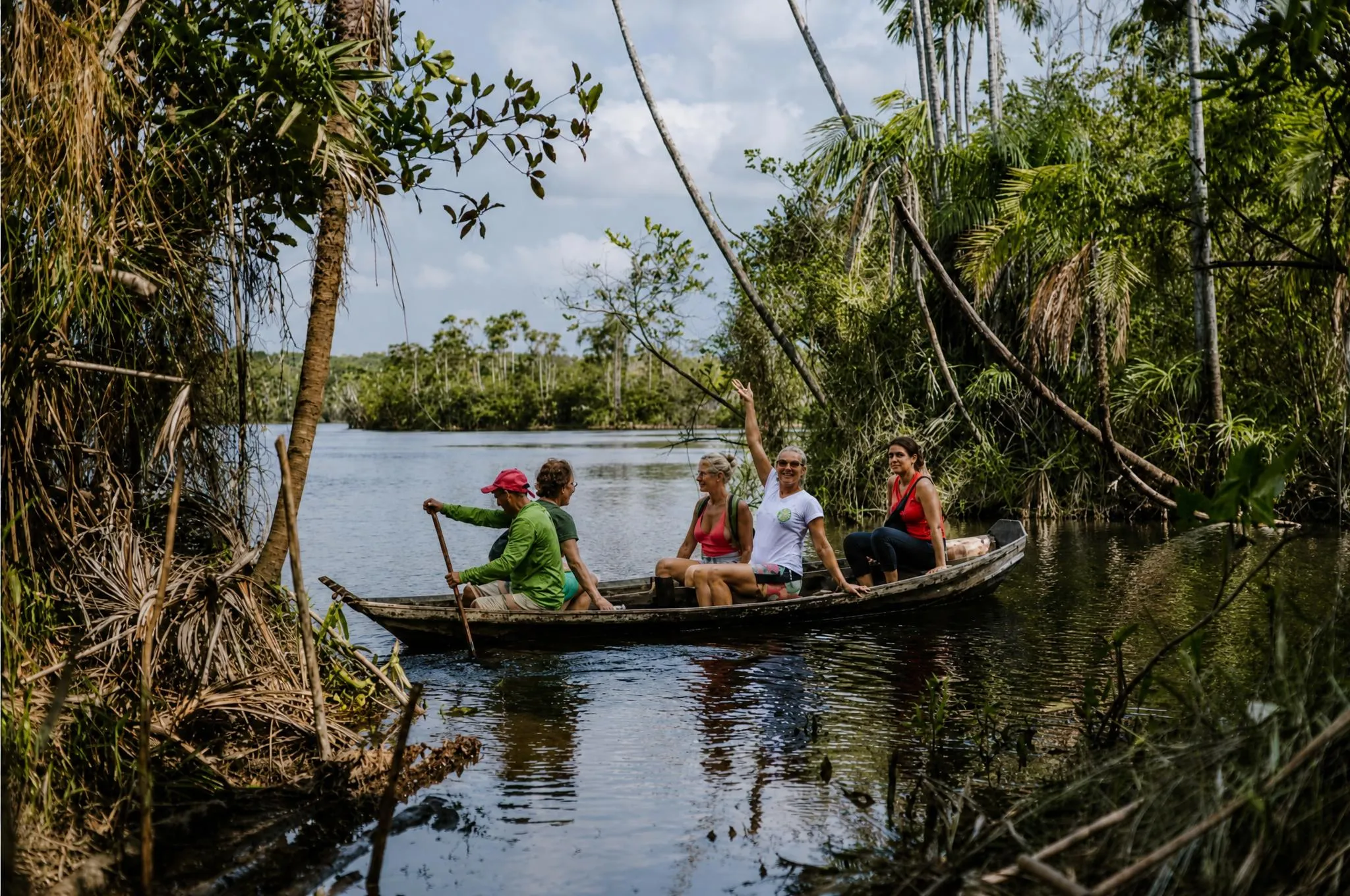 Cuatro personas dentro de una canoa de madera en el igapó, entre troncos sumergidos y lianas, sobre agua oscura y quieta