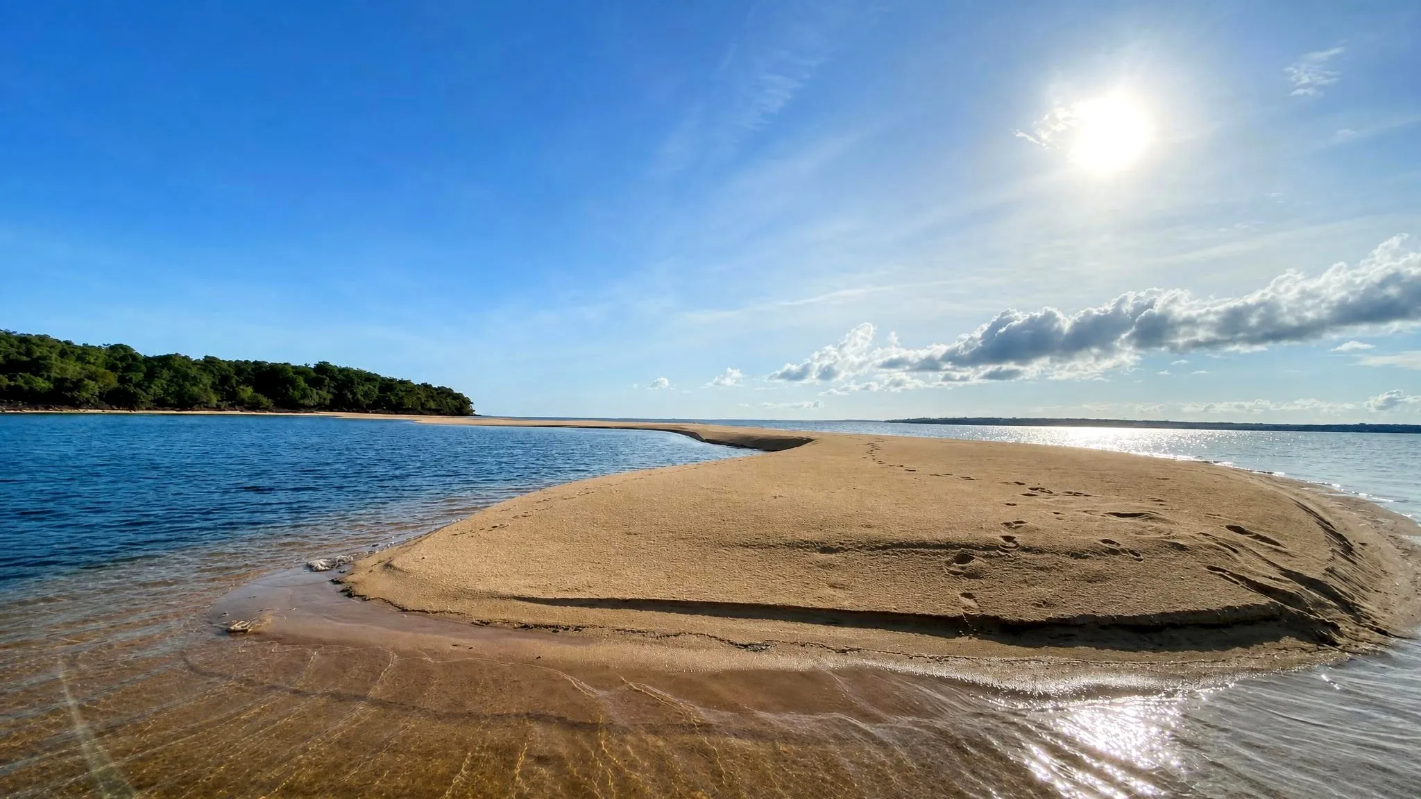 Banco de areia baixo no meio do rio, com o sol alto no céu e a água rasa transparente mostrando o fundo